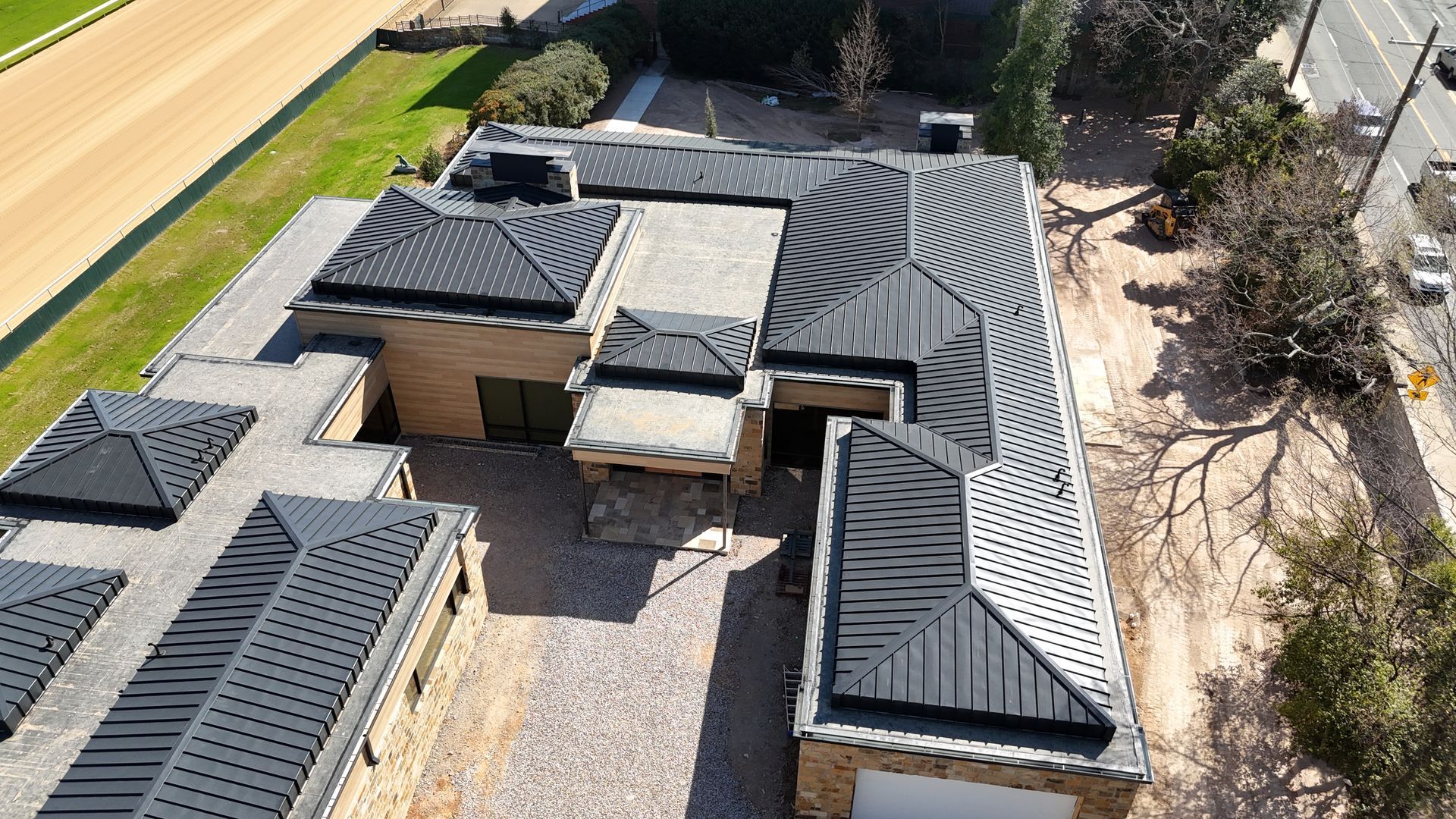 Aerial view of a house with a dark gray roof and stone walls next to a road.