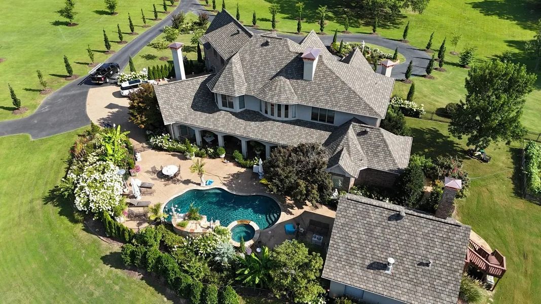 Aerial view of a large home with a pool, surrounded by green lawns and trees.