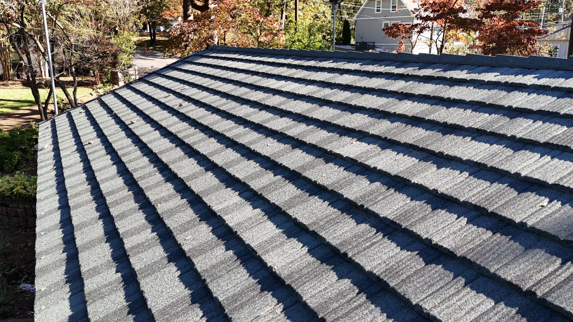 Gray shingle roof, angled view. Sunlight, trees in background, autumn.