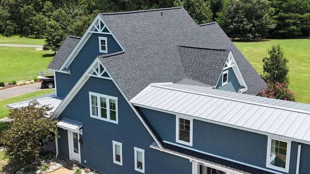 Blue house with dark gray shingle roof and white trim, set in a grassy yard.
