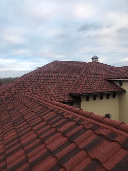Red tile roof with dark shadowing under cloudy sky.