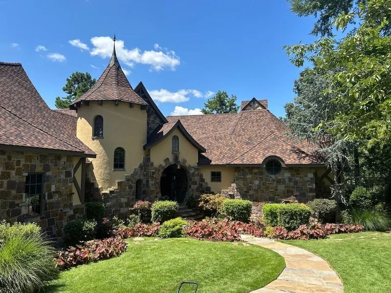 Stone and yellow castle-like home with a curved path, green lawn, and red flowers under a blue sky.