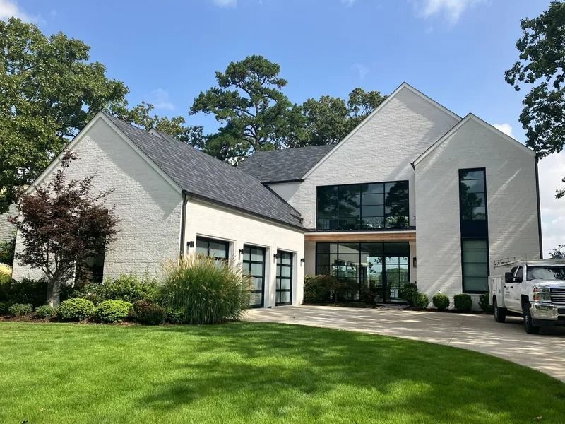 Modern white brick house with black framed windows, black garage doors, and a green lawn.