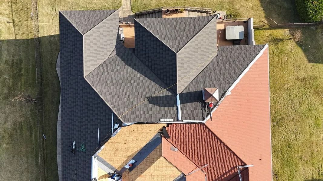 Overhead view of a house with multi-colored roof sections: gray shingles, red tiles, and tan areas.
