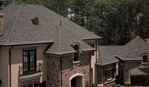 Stone and stucco house with a multi-angled, brown shingled roof and arched windows.