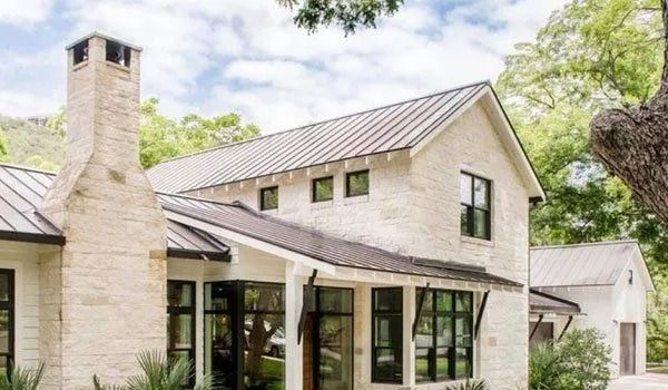 Modern farmhouse with stone exterior, metal roof, and black-framed windows.
