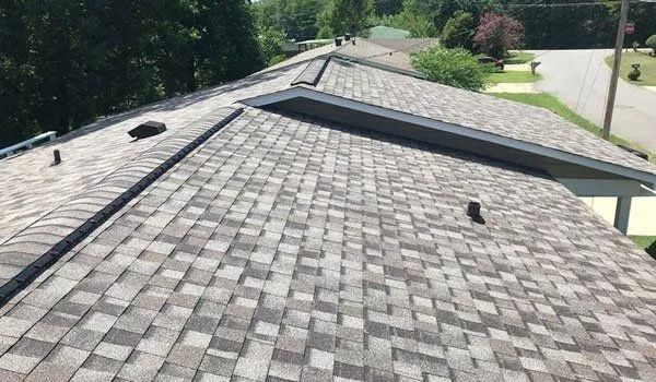 A shingled roof with multiple sections, viewed from above, in a residential area.