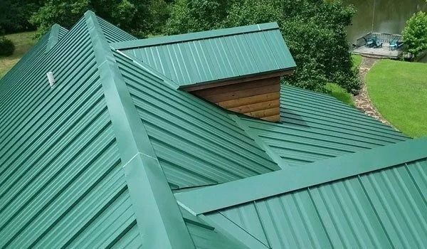 Green metal roof with ridges, on a house, with a wooden chimney.