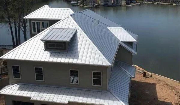 House with a shiny metal roof overlooking a lake.