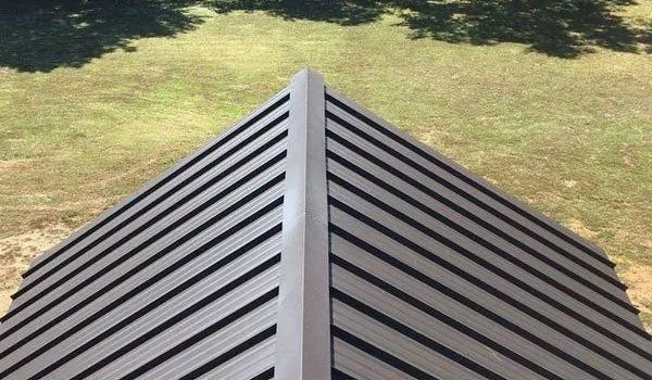 Overhead view of a metal roof with a central ridge against a green grassy background.