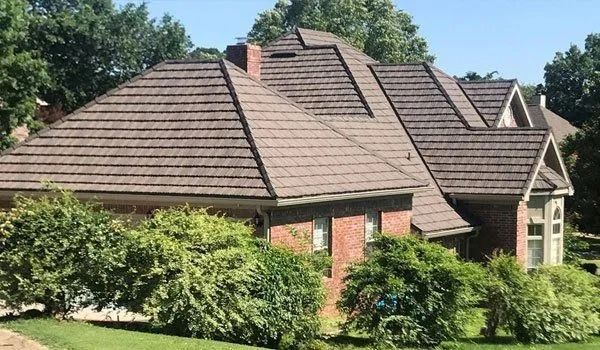 Brown roof on a brick house, obscured by green bushes.