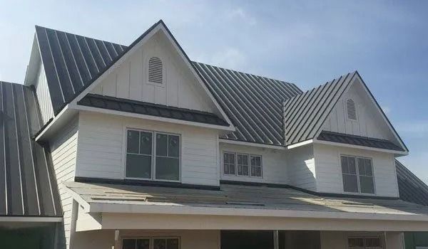 White house with dark metal roof; two-story with multiple gables. Blue sky in the background.