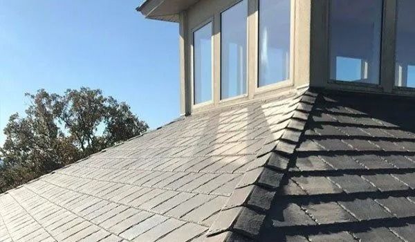 Slate roof on a building with windows. Blue sky, trees.