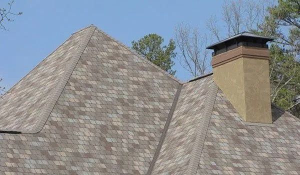 Tan and brown shingle roof with chimney against a blue sky.