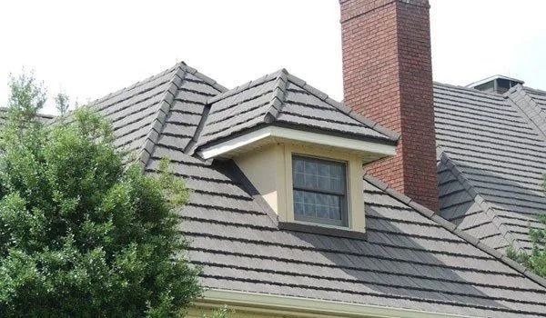 Gray tiled roof with dormer window; red brick chimney rises in the background.