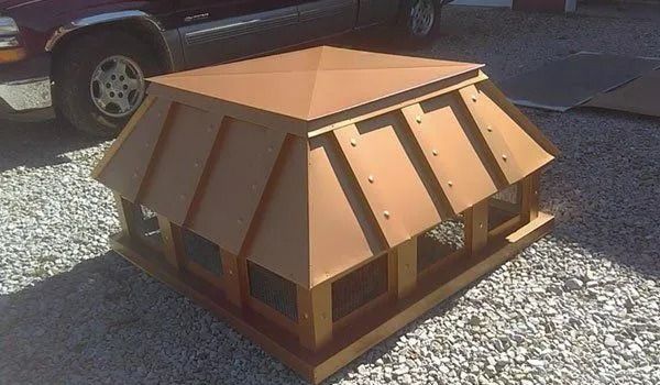 Copper-roofed gazebo structure on gravel; adjacent to a vehicle. Brown, square, and outdoors.