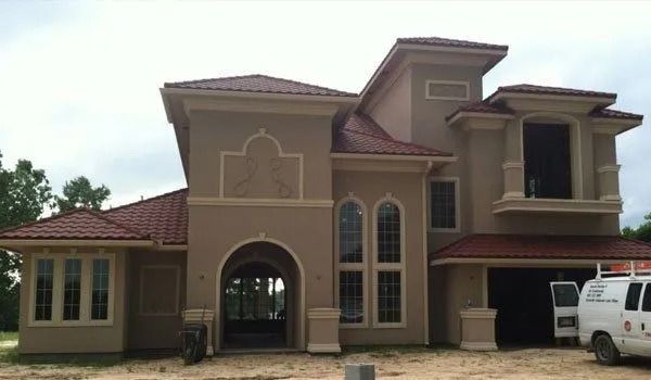 Tan stucco house with red-tiled roof and arched entryway; a white van is parked in the driveway.