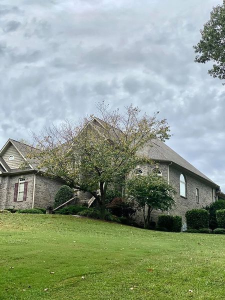 Brick house with gray roof on a grassy hill under an overcast sky