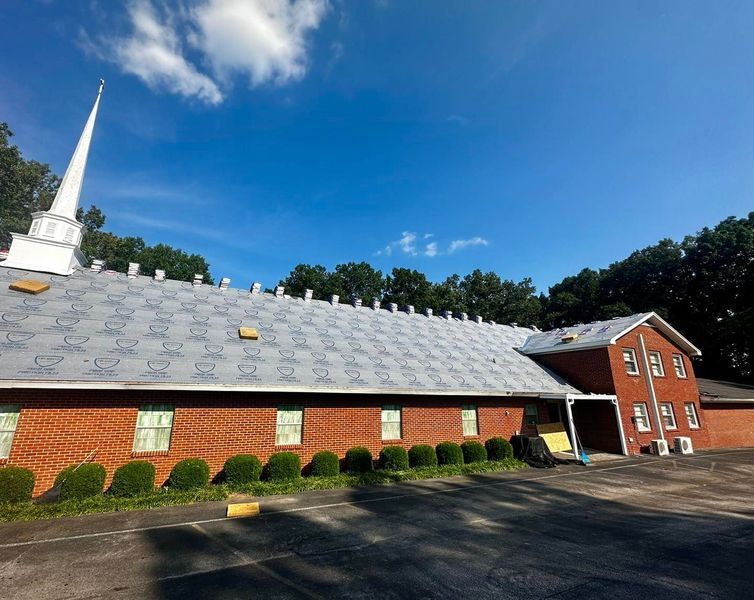 Red brick church with white steeple and gray roof under a clear blue sky