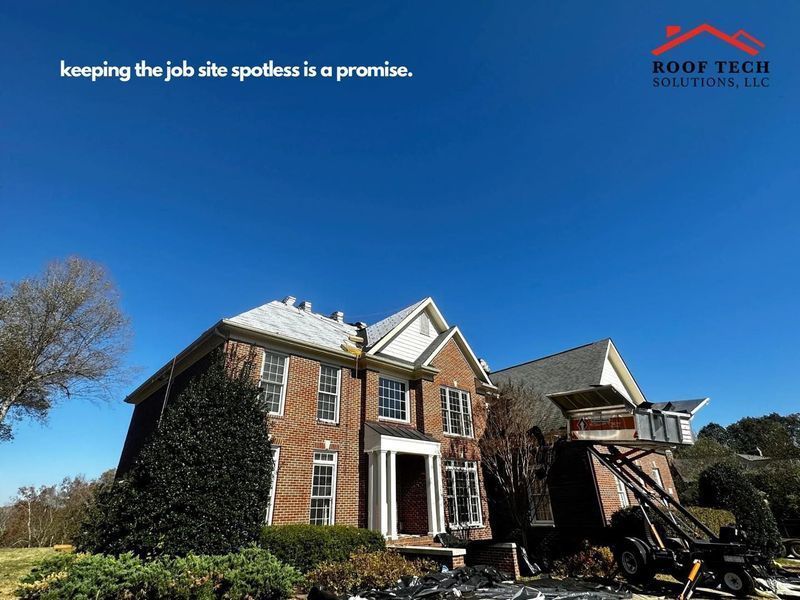 Brick house roof being cleaned by a work truck under a clear blue sky