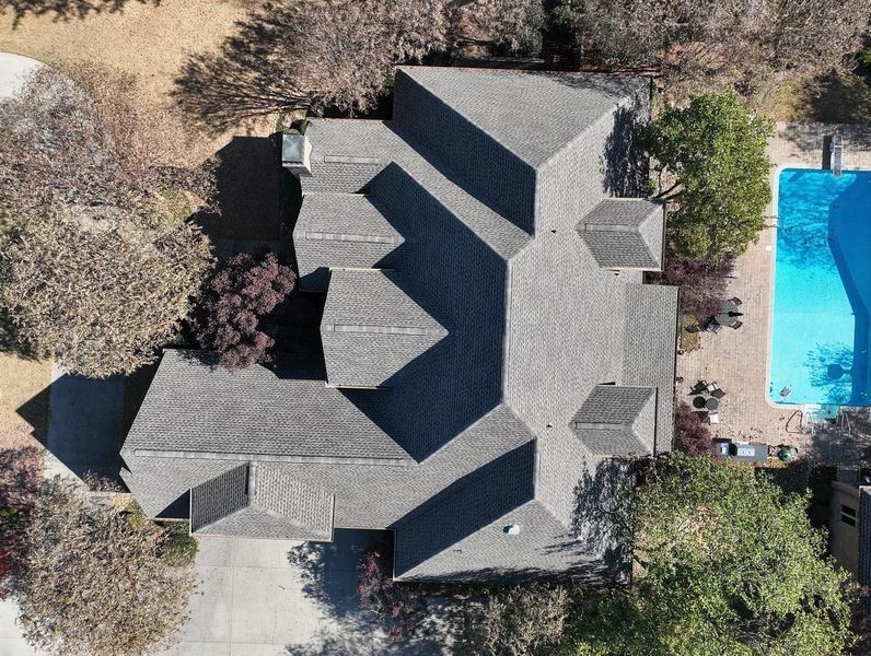 Aerial view of a gray-roofed house beside a bright blue swimming pool and surrounding trees.