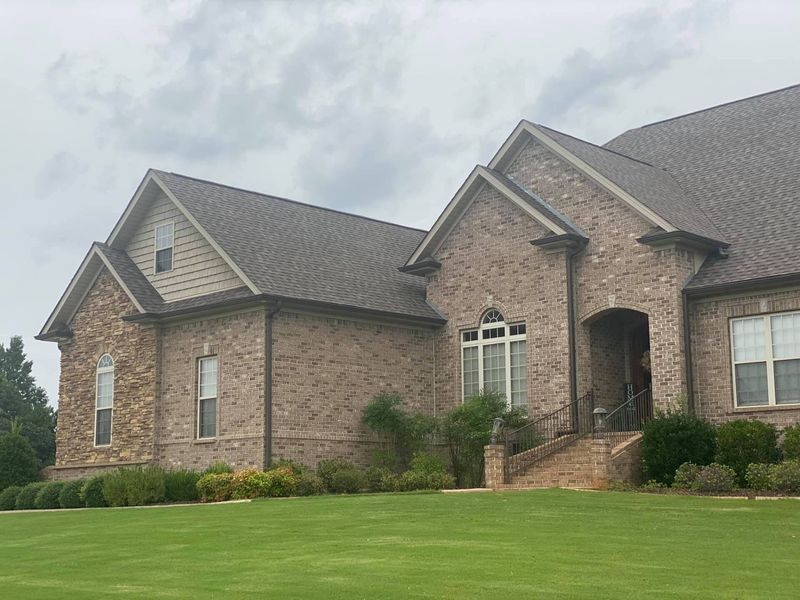 Brick suburban house with a manicured green lawn and cloudy sky