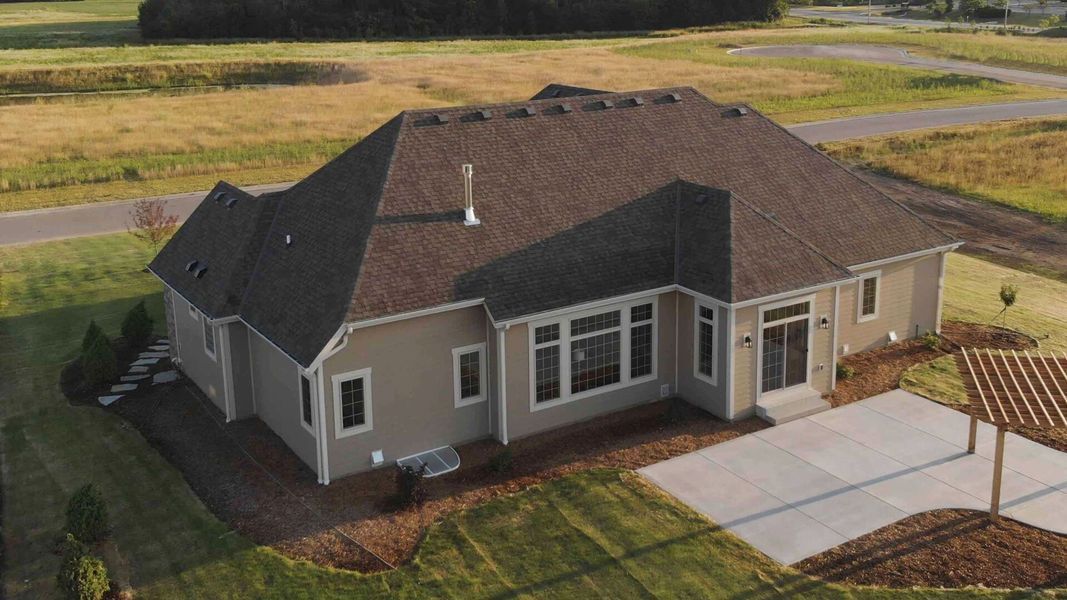 Aerial view of a tan suburban house with a dark roof, driveway, and lawn