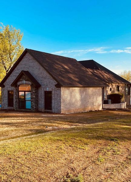Small stone house with a brown roof on a grassy lot under a clear blue sky