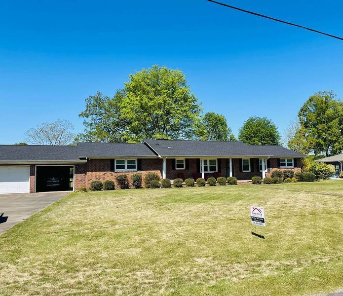 Single-story brick house with green lawn, garage, and blue sky