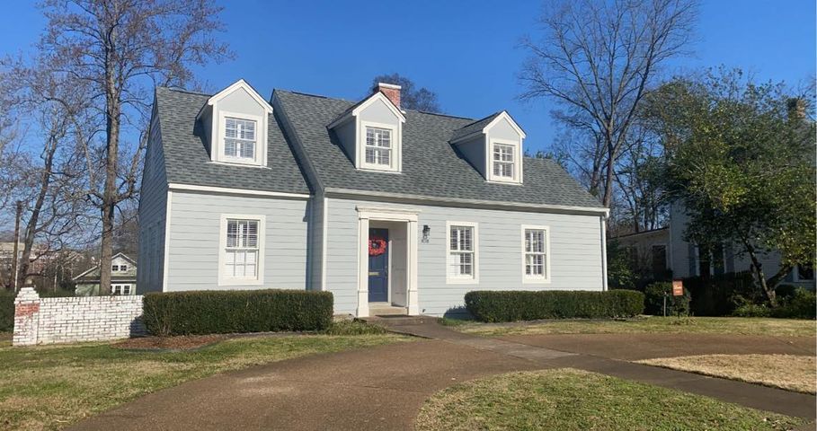 White farmhouse with three dormer windows, red front door, and lawn under a clear blue sky