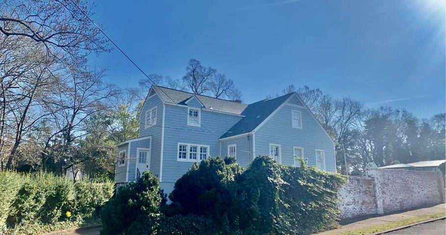 Blue two-story house with white trim beside a stone wall, framed by trees under a clear sky.
