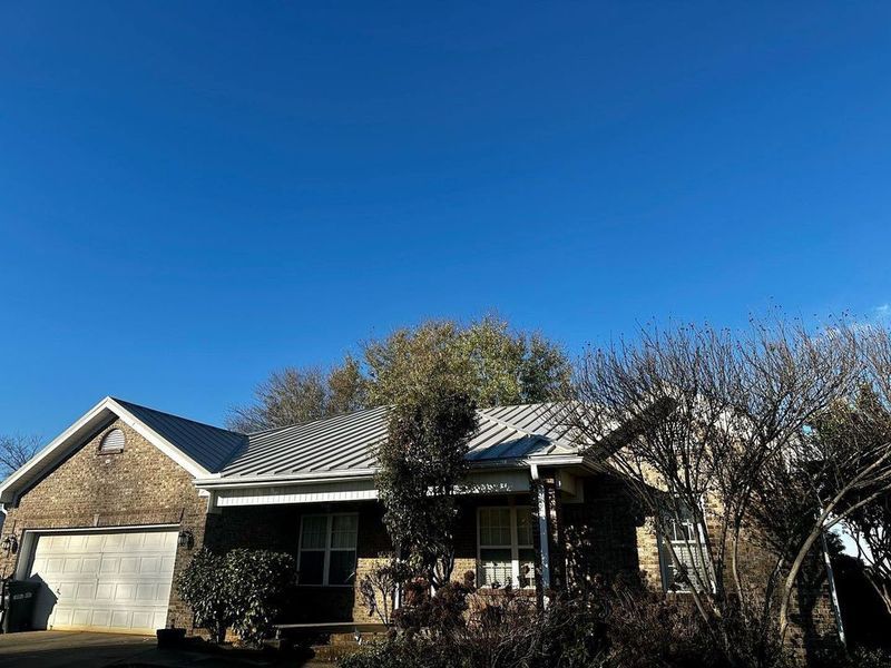 Single-story brick house with gray roof and bare trees under a clear blue sky