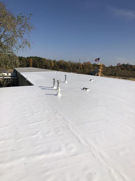 Flat white roof with vents under a clear blue sky, trees and an American flag in the distance