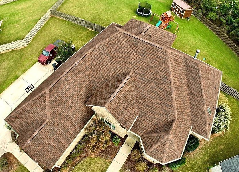 Aerial view of a brown-roofed house with lawn, driveway, and backyard patio furniture.