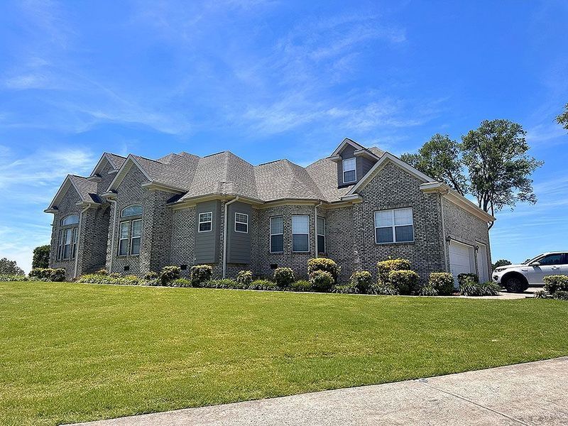 Large stone suburban house with a manicured lawn under a bright blue sky