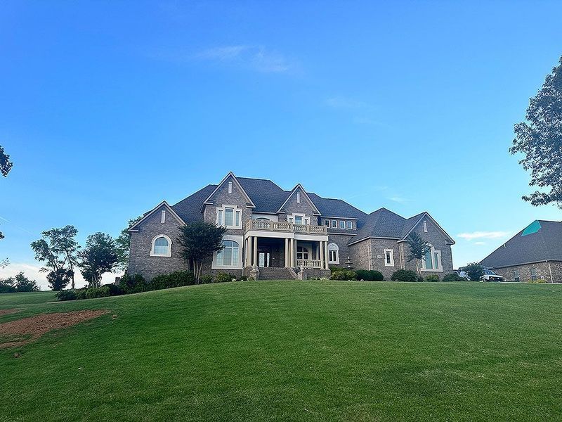 Large stone house with a spacious green lawn under a blue sky