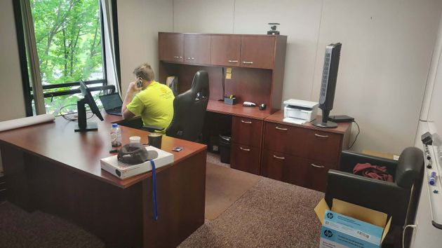 Office with a person in a neon yellow jacket seated at a desk, surrounded by cabinets and papers.