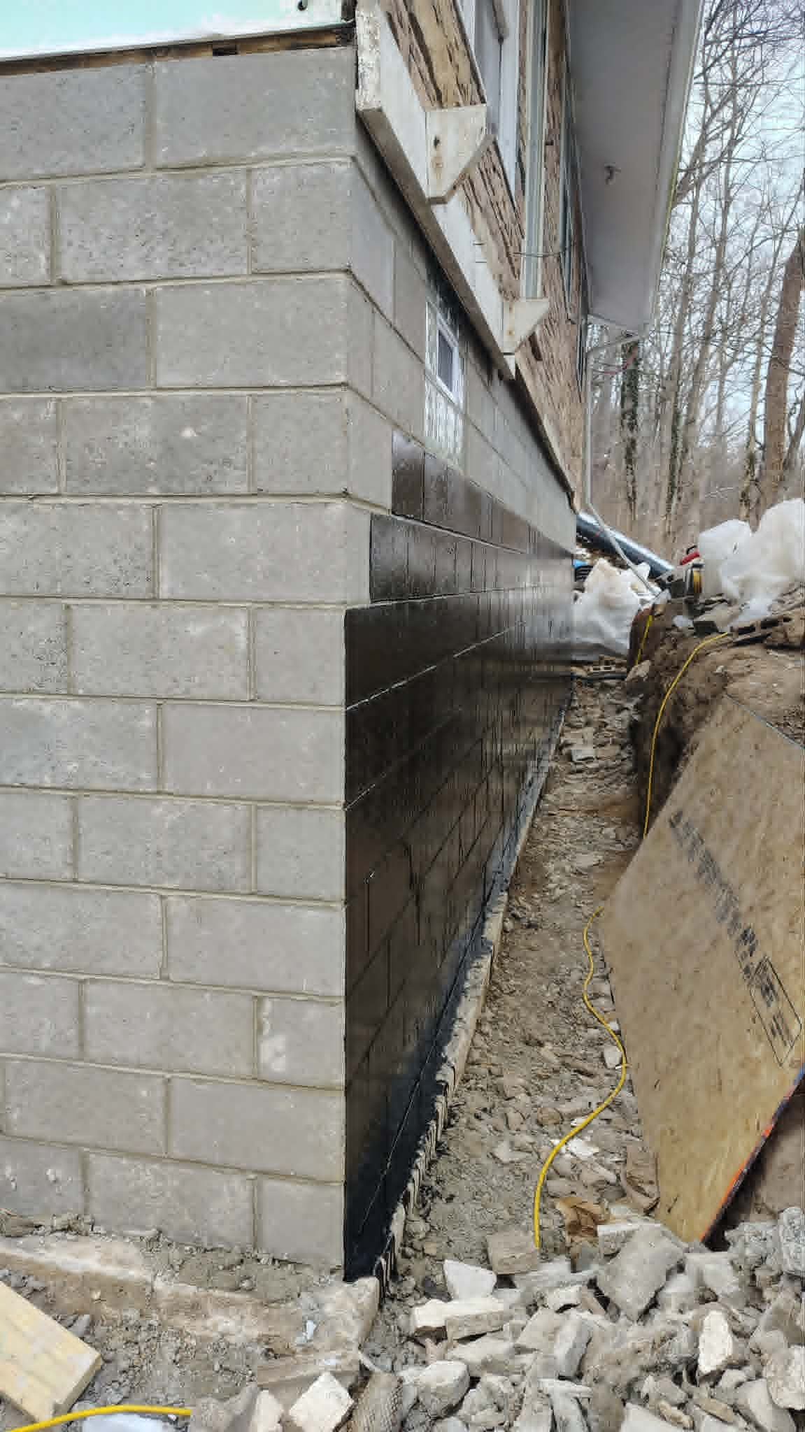 Flood damage beside a cinder block building, with a narrow water-filled trench and debris along the edge