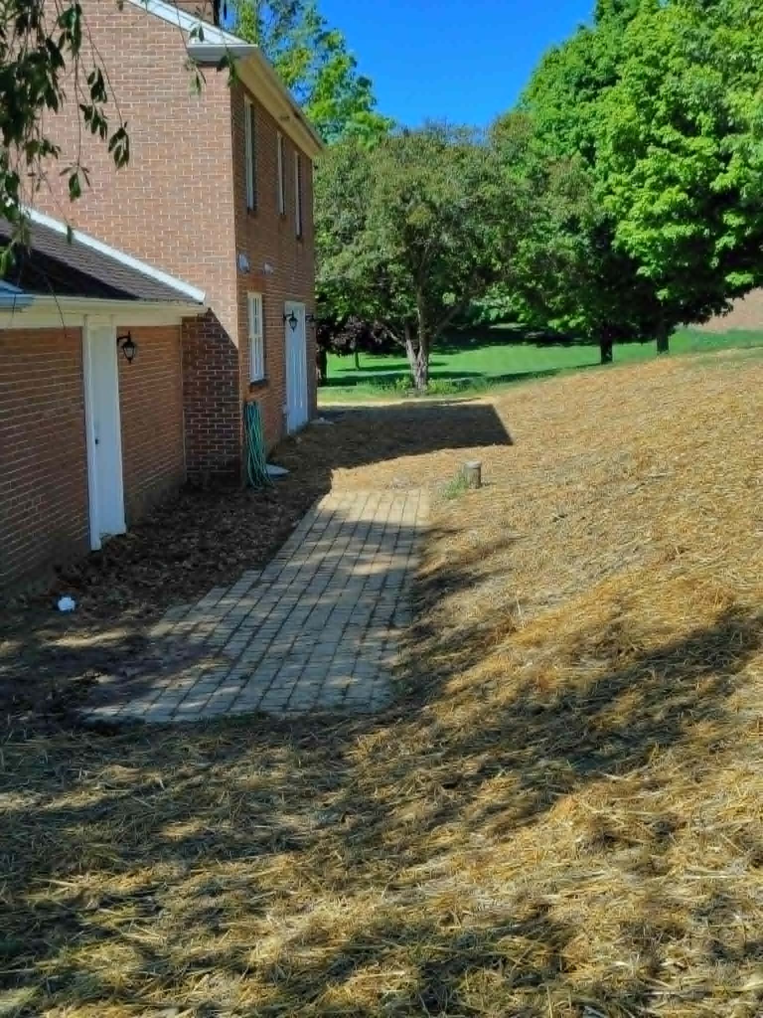 Brick apartment building beside a paved walkway and grassy slope under bright blue sky