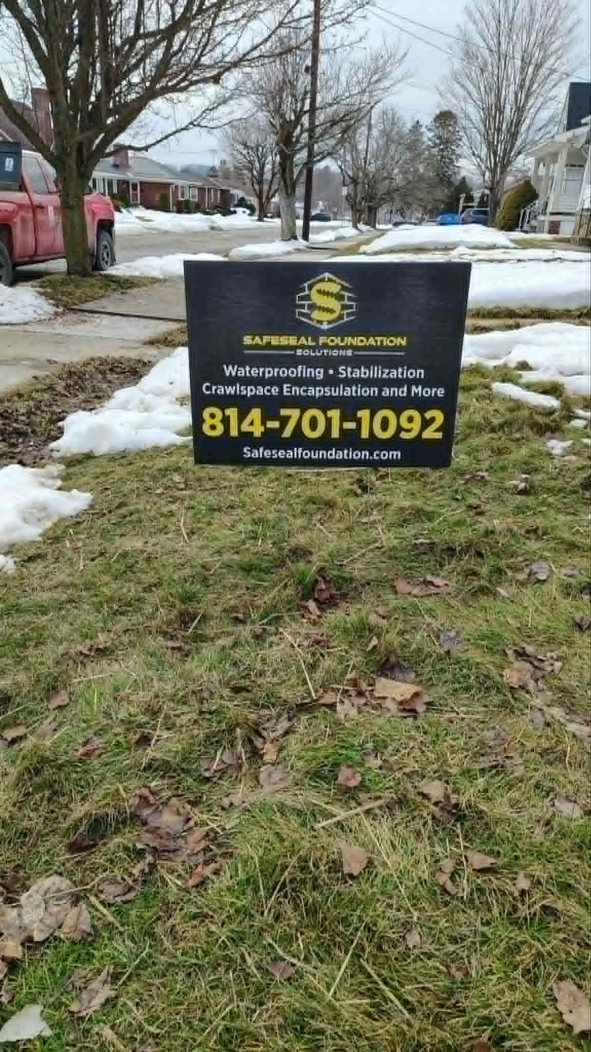 Black yard sign on snowy lawn advertising plumbing services with phone number 814-701-1092.