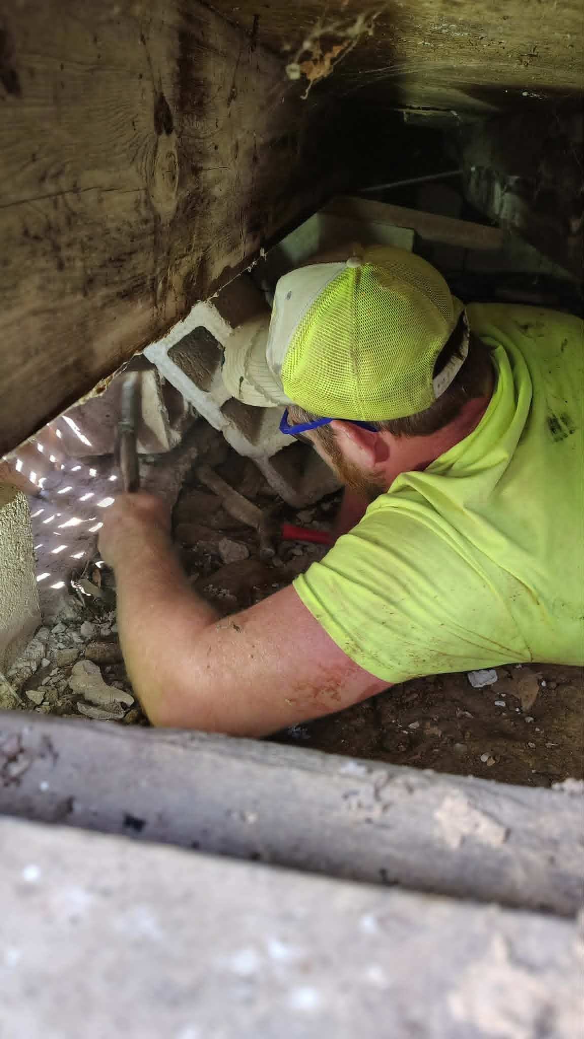 Worker in neon green shirt and cap crouches inside a dark pipe, inspecting or repairing equipment.