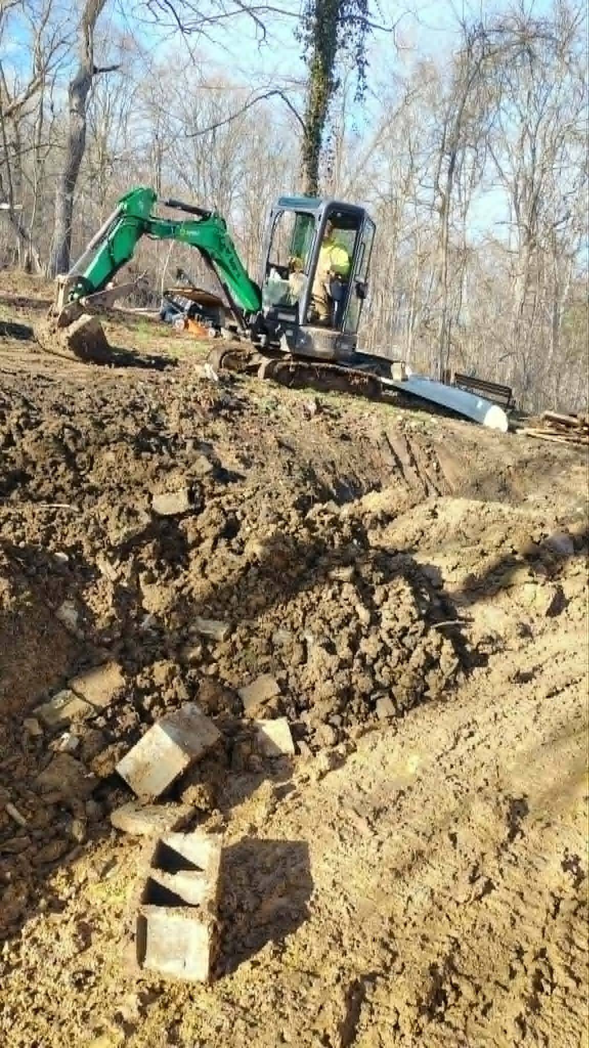 Green excavator digging a dirt hillside in a wooded construction area