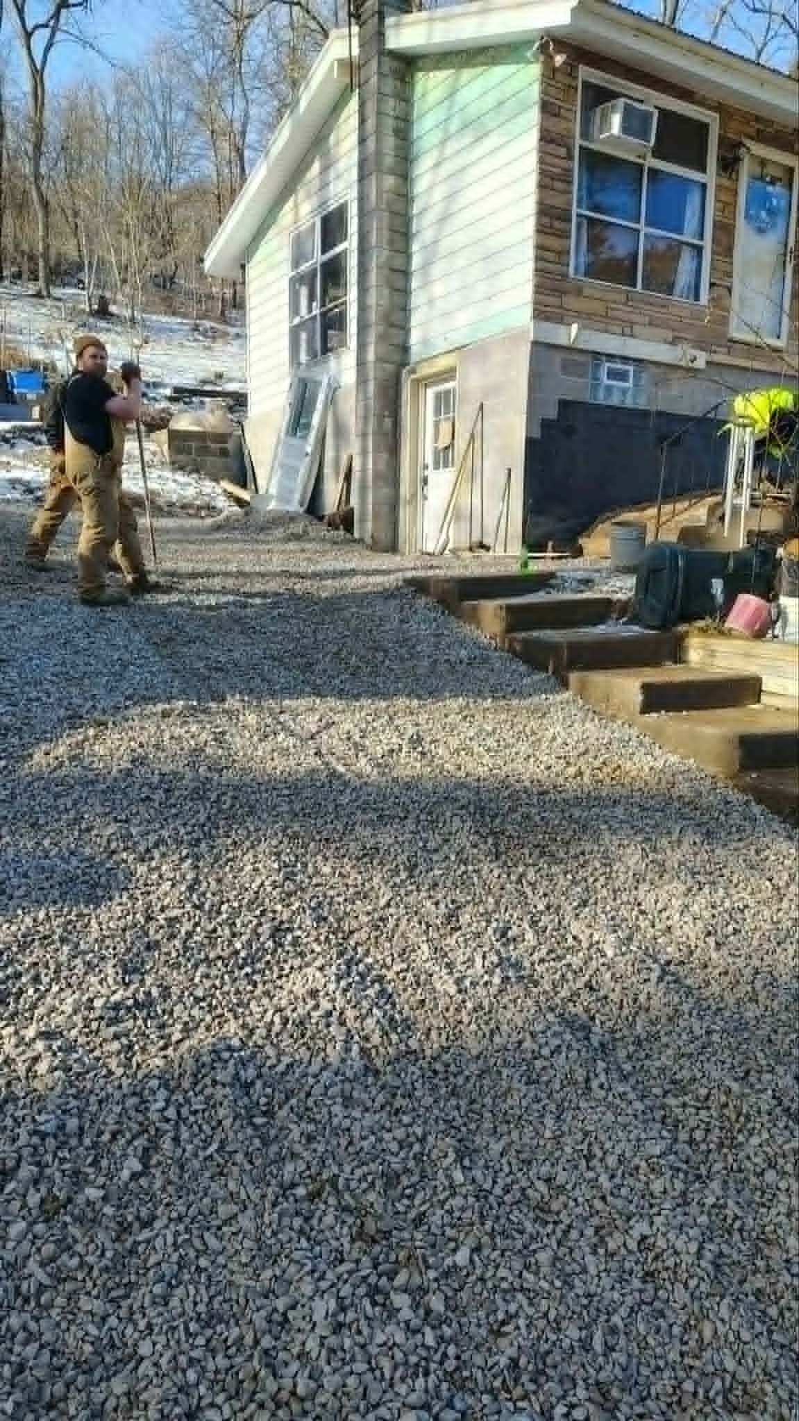 Construction workers grading a gravel driveway beside a small house on a sunny day