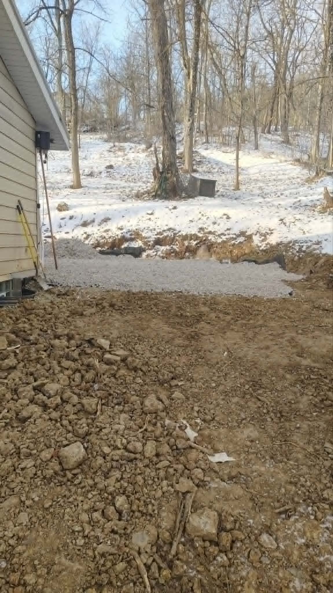 Snowy backyard beside a house with bare trees and a patch of dirt in the foreground