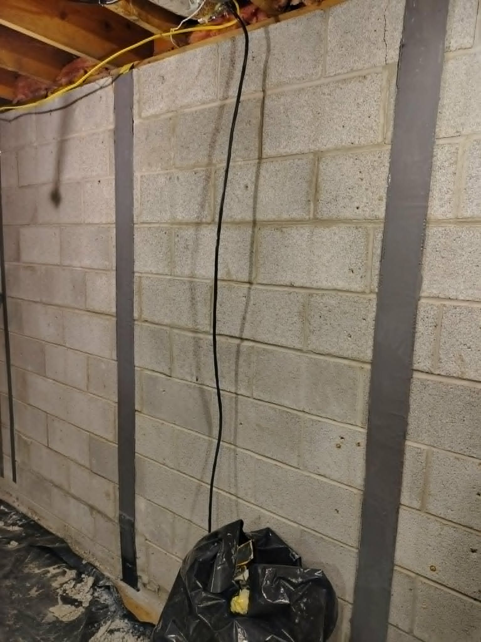 Basement cinder block wall with hanging cable and a black trash bag on the floor