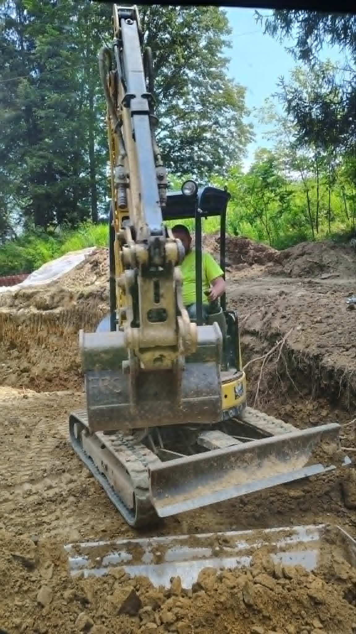 Yellow excavator digging in a muddy construction site surrounded by soil piles and trees