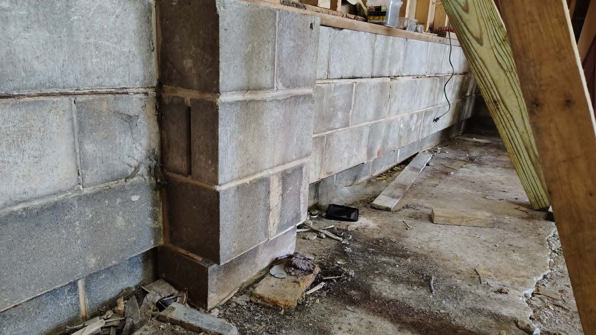 Cinder block wall under construction with wooden supports in a narrow dirt space