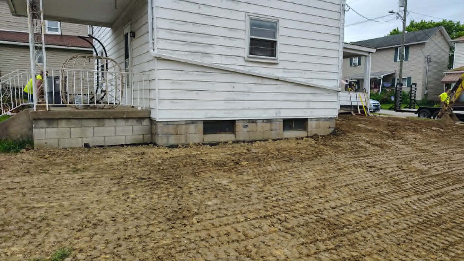 Backyard beside a white house with bare dirt and a small porch on a cloudy day