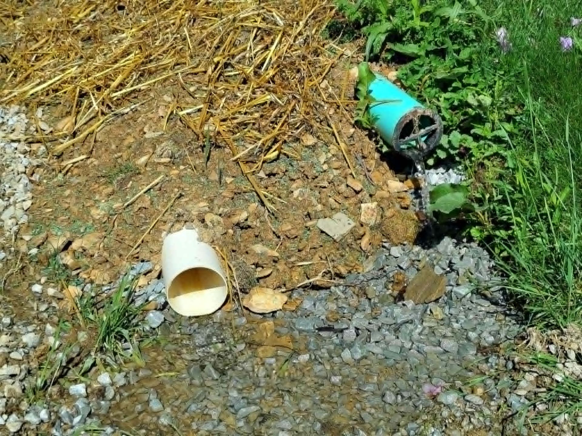 Two tipped-over plastic cups on gravel beside a grassy drainage ditch with muddy water