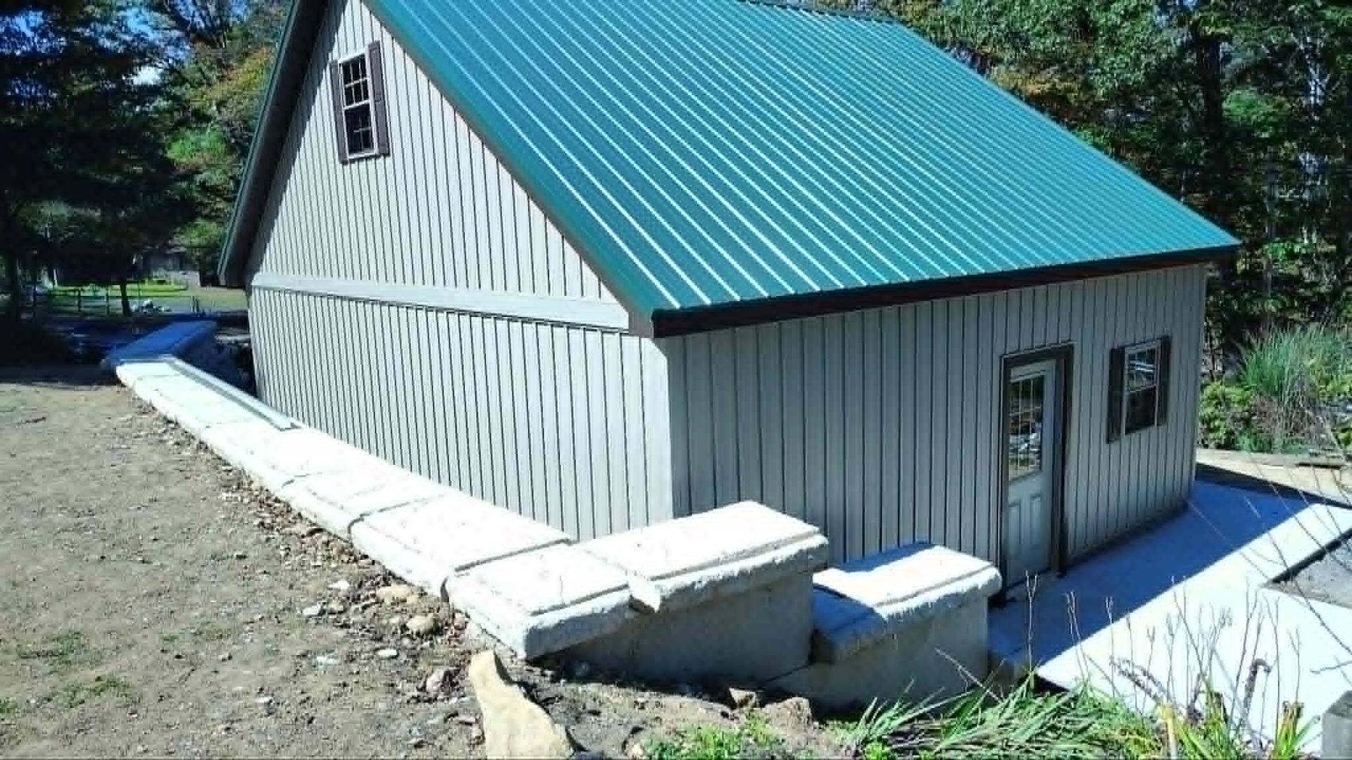 Small white cabin with a green metal roof on a hillside, viewed from the side.